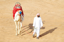 a man in a desert walking a camel 