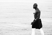 a shirtless muscular man walking on a football field 