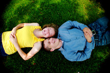 Boy and girl laying opposite of each other in the grass; their heads touching