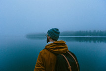 man standing with a backpack in front of a lake in winter 