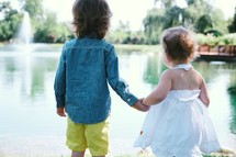 toddlers holding hands by a pond