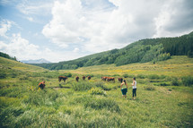 women near cows grazing in a pasture 