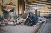 A woman sits on the floor in prayer in an abandoned house.
