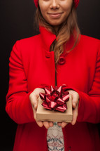 a woman in a red trench coat holding a gift box 