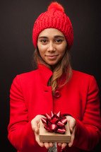 a woman in a red winter hat and coat holding a Christmas gift 