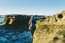 Woman with a backpack walking along rocks in the ocean.