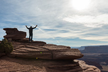 man standing on a mountain top with raised hands 