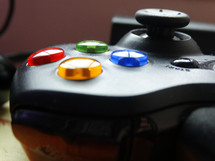 Close up of blue, green and yellow buttons next to thumb stick on black video game controller; game night concept