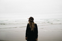 woman standing on a beach with a hat and long blonde hair 