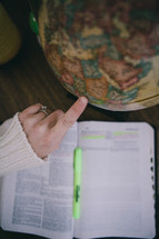 finger pointing to a globe and an open Bible 
