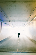 a man walking through a tunnel of a parking garage 