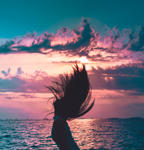 woman flipping her hair in front of a sunset view of the ocean 