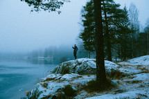 man standing on a rock by a lake in winter 