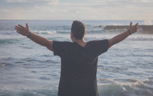 a man with open arms standing near the ocean 