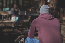 A man in a beanie sitting by the campfire
