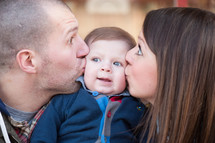 a mother and father kissing their infant son on the cheeks 