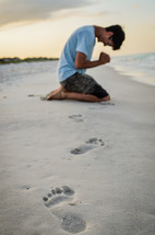man kneeling in prayer on a beach