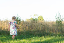 toddler girl exploring a grass field 