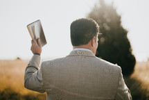 a man holding up a Bible outdoors 