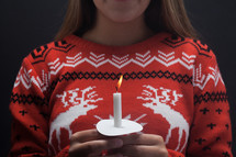 girl in a Christmas sweater holding a candle 
