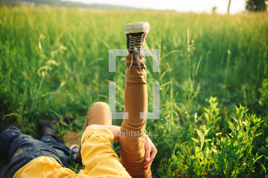 woman and man having fun outdoors. Loving hipster couple walking in the field, kissing and holding hands, hugging, lying in the grass and lifting their legs up in the summer at sunset. valentines day.