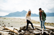  a couple walking around driftwood on a shore 