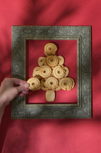 Hand placing cookies in a Christmas tree within a frame