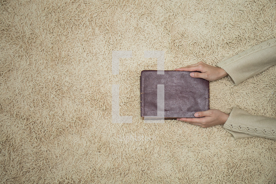 a woman holding a Bible over a rug 