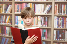Boy reading a book in a library.
