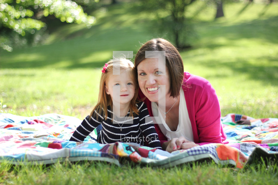 Mother and daughter laying on a blanket in the grass outside