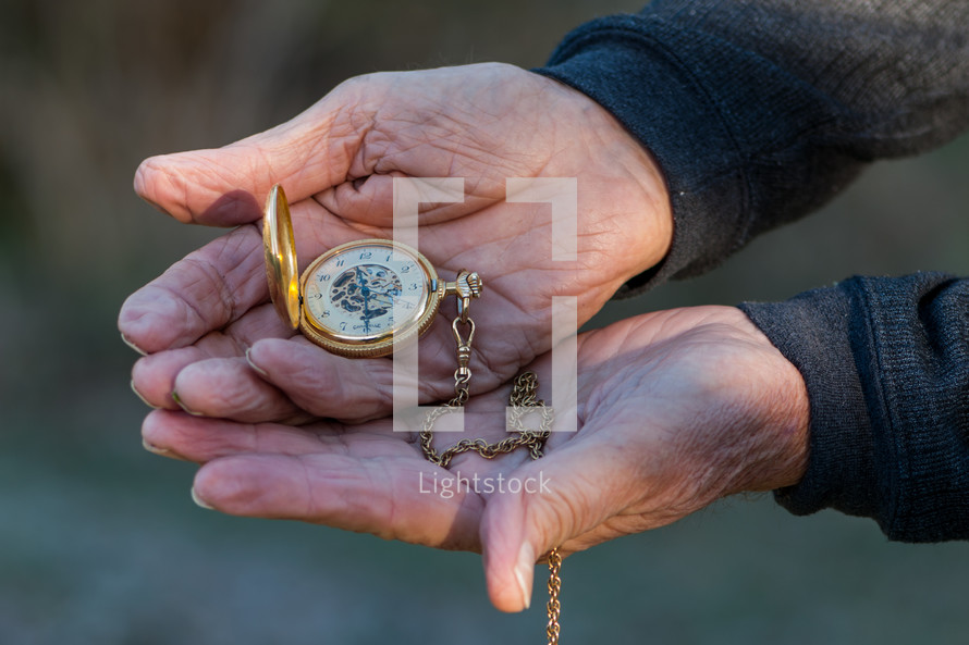 elderly hands holding a pocket watch 
