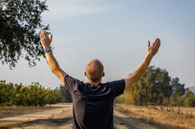 man with arms raised in worship standing on railroad tracks 
