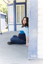 Pregnant woman sitting on the ground leaning against a house.