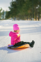 a child in a winter coat sitting on a sled in the snow 