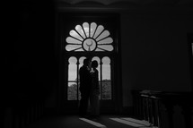 Silhouette of a man and woman standing before an ornate window.
