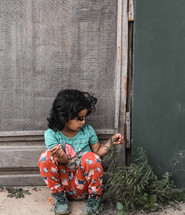 a little girl playing with weeds growing in cracks in the sidewalk 