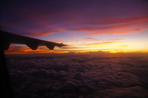 Airplane wing over clouds at sunset, sunrise, dusk, dawn