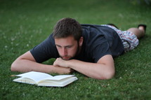 man lying in the grass reading a Bible 