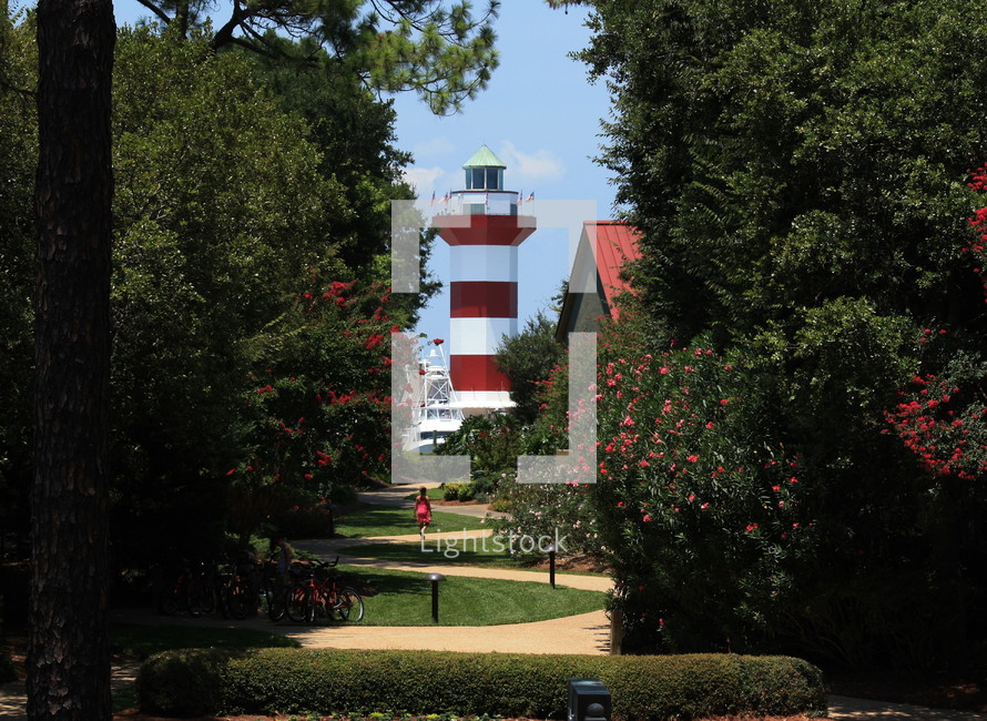 a lighthouse, seen at the end of a winding path through a garden surroundings