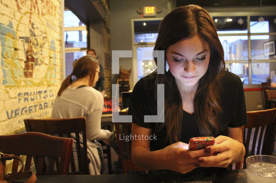  a young woman sitting at a diner table texting 