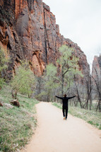 man walking along a paved path and red rock cliffs 