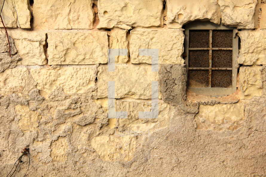 Barred window in weathered stone wall 