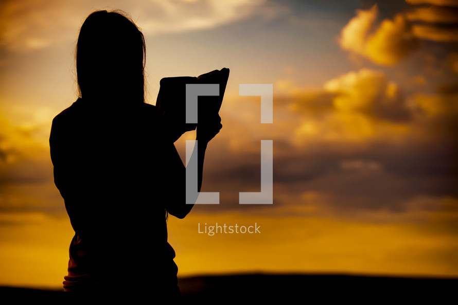 Girl reading the Bible at sunset silhouette