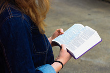 a teen girl in a jean jacket reading a Bible 