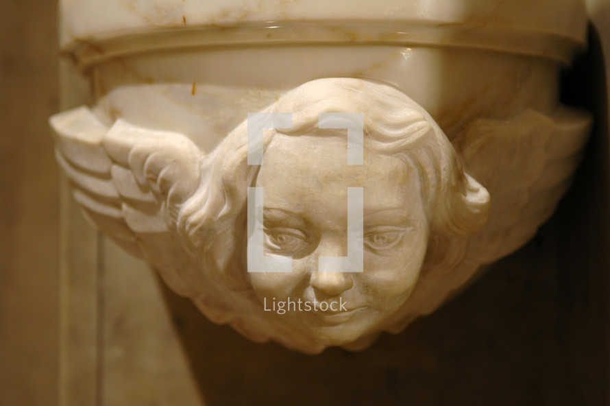 Marble face and wings of an gothic angel on a column