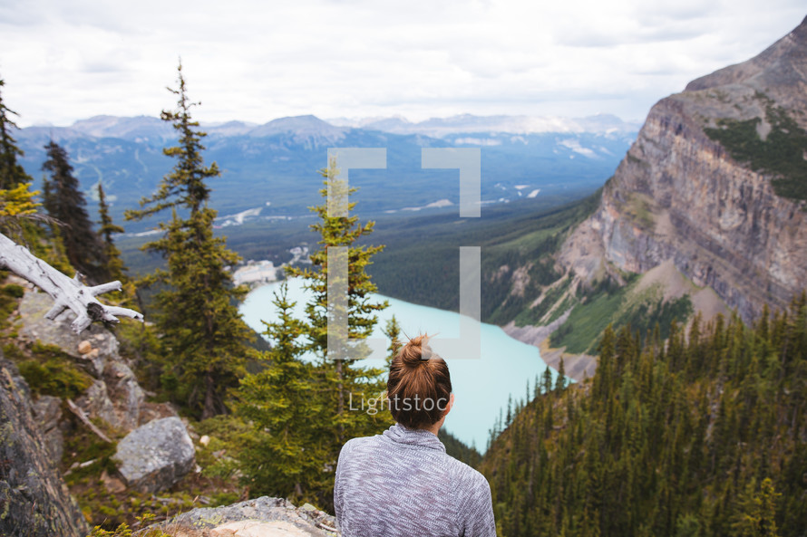A woman sitting on a mountaintop looking out at the view 