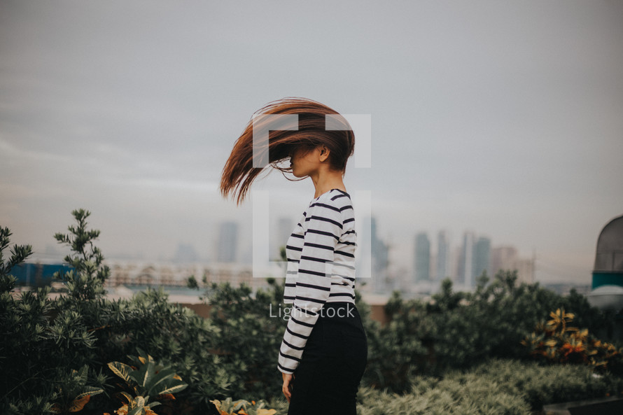 a woman flipping her hair and city view in the background 