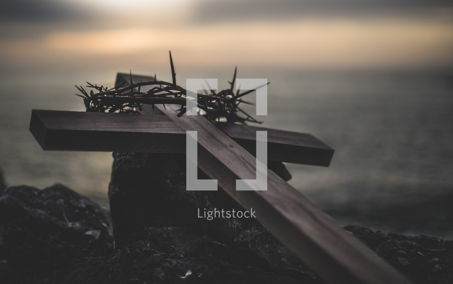 wooden cross and crown of thorns on a rock at sunset 