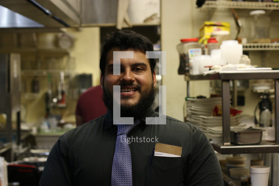A smiling man standing in a restaurant kitchen.