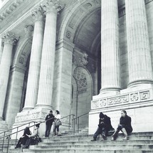 people sitting on the stairs in front of a building with large columns and arches 